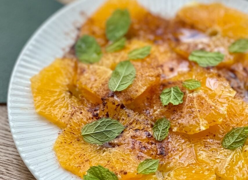 Mediterranean orange carpaccio with olive oil, cinnamon, and mint on a white plate.